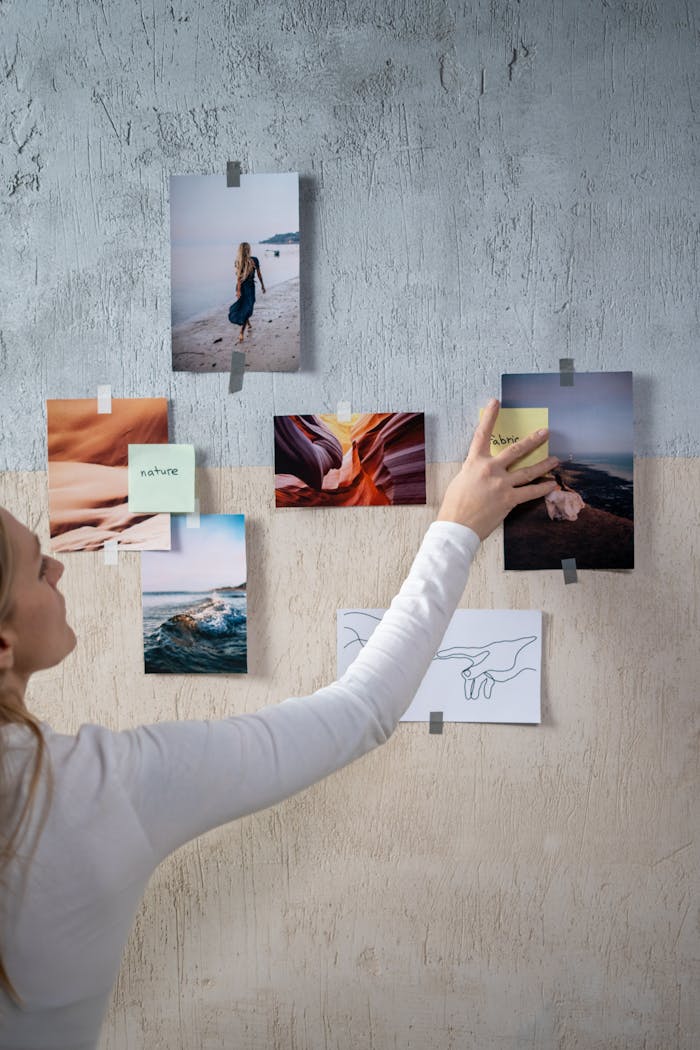 A woman arranging photos and sticky notes on a textured wall, enhancing a creative moodboard.